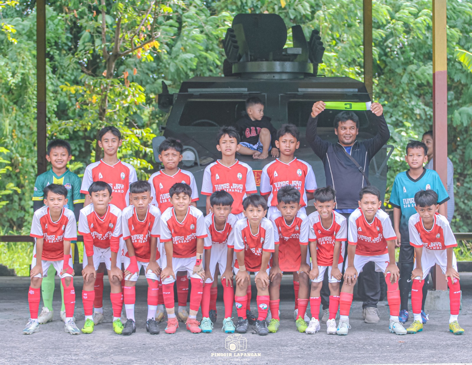 Pemain Tunas Jaya Sepande U-12 bersama CEO Zainuri di depan sebuah kendaraan militer sebelum tampil di Piala Askab PSSI Sidoarjo di Lapangan Panser, Sumput, Sidoarjo, Sabtu (18/10/2025).